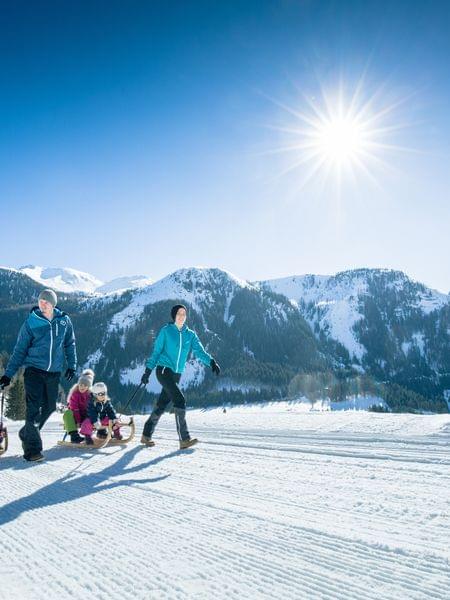 Rodeln Obertauern Familie wandert mit Schlitten im sonnigen Winterurlaub in den verschneiten Alpen